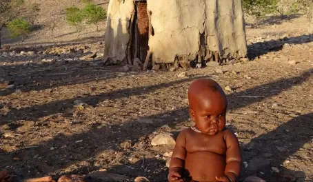 A young child sits in front of a African hut