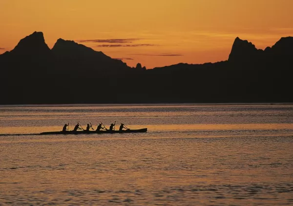 Locals paddle a traditional canoe at sunset