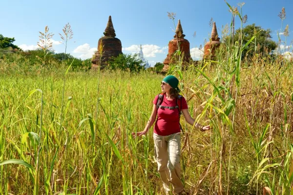 A backpacker walking and looking across field to ancient buddhist stupas